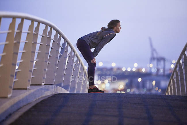 Female runner resting on urban footbridge at dawn — Stock Photo
