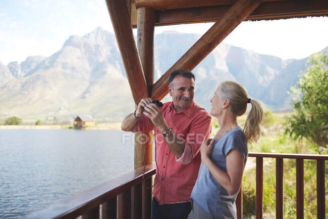 Happy couple with binoculars enjoying lake view from balcony — Stock Photo