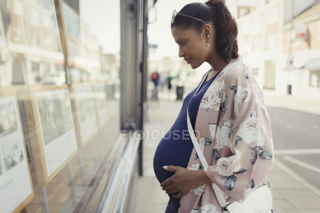 Pregnant woman browsing real estate listings at urban storefront — Stock Photo