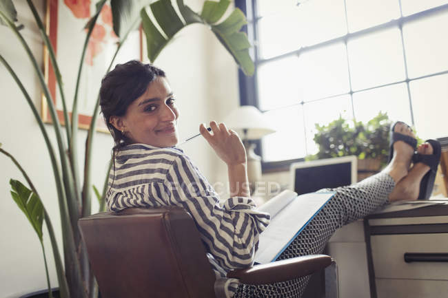 Портрет уверенной в себе деловой женщины, работающей, рассматривающей документы с ногами на столе — стоковое фото