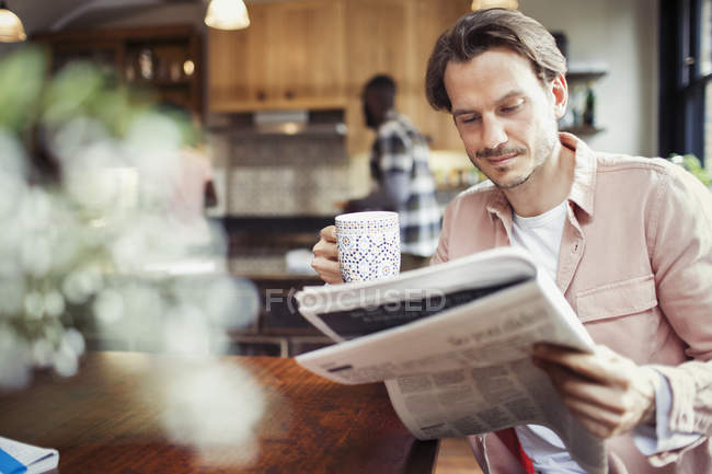 Uomo che beve caffè e legge giornali in cucina — Foto stock