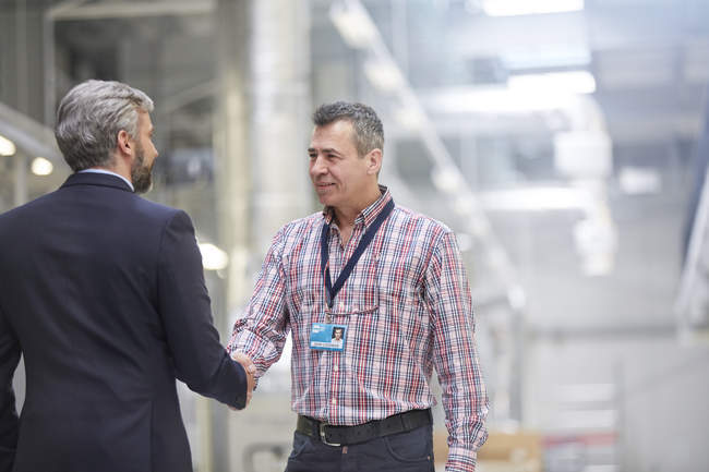 Businessman and supervisor handshaking in factory — Stock Photo
