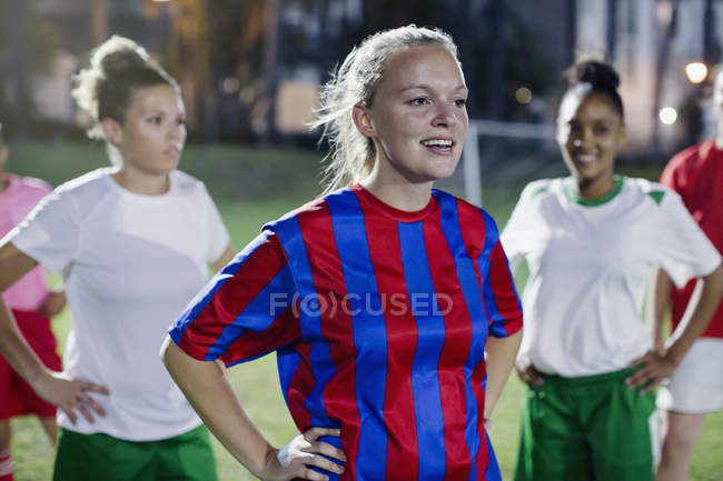 Jovens jogadoras de futebol confiantes descansando com as mãos nos quadris no campo à noite — Fotografia de Stock