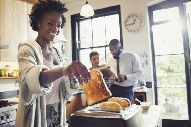 Улыбающаяся женщина тостит хлеб в тостере на кухне — стоковое фото