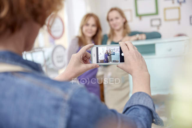 Mulher com câmera telefone fotografar colegas posando na mesa lateral pintada em oficina de aula de arte — Fotografia de Stock