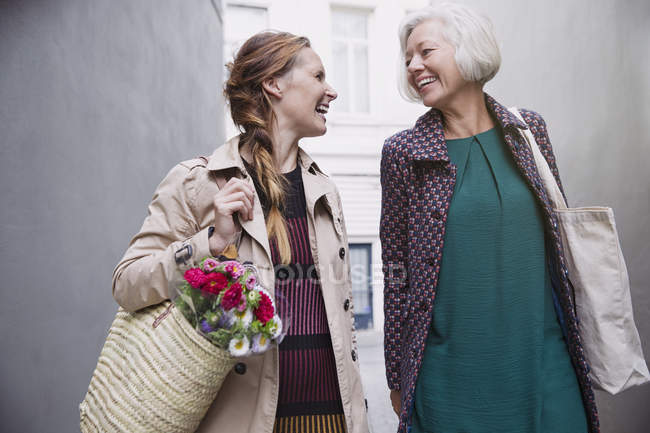 Sonriente madre e hija con bolsas de compras en el callejón - foto de stock