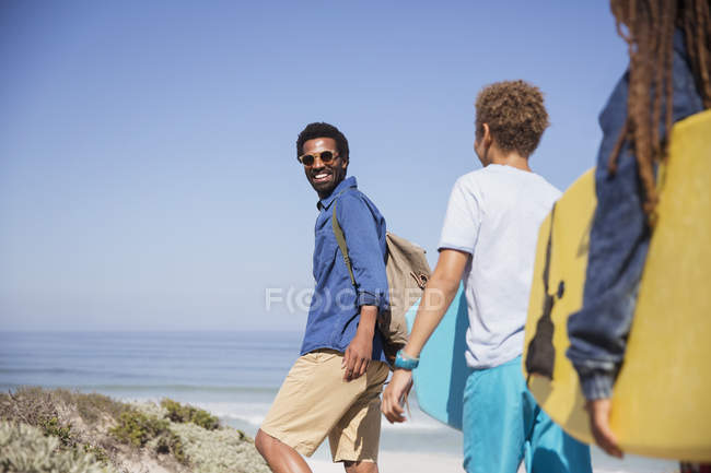 Портрет улыбающийся отец и дети с буги-досками прогуливаясь по солнечному летнему пляжу — стоковое фото