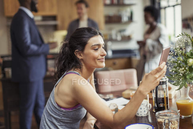 Mulher jovem mensagens de texto com telefone inteligente na mesa de café da manhã — Fotografia de Stock