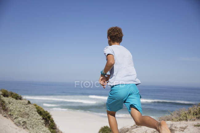 Pre-adolescent boy running on sunny summer ocean beach — Stock Photo
