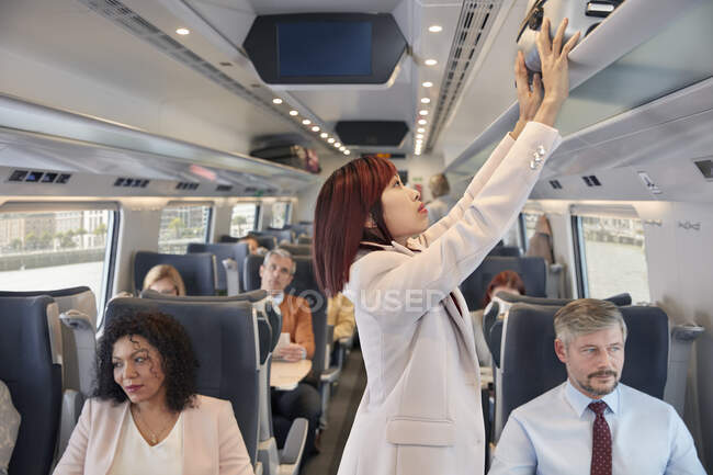 Maleta de mujer de negocios guardando en el compartimento superior del tren de pasajeros - foto de stock