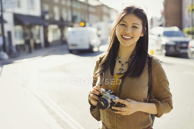 Портрет усміхнений, впевнена молода жінка-туристка з фотоапаратом на сонячній міській вулиці — стокове фото