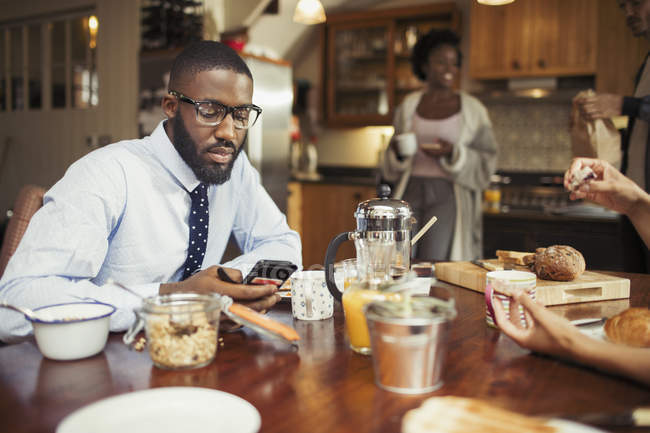 Geschäftsmann textet mit Smartphone am Frühstückstisch — Stockfoto