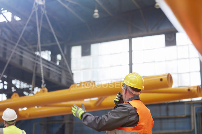 Male worker with walkie-talkie guiding lowering of equipment in factory — Stock Photo