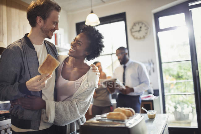 Affectionate couple hugging and eating toast in morning kitchen — Stock Photo
