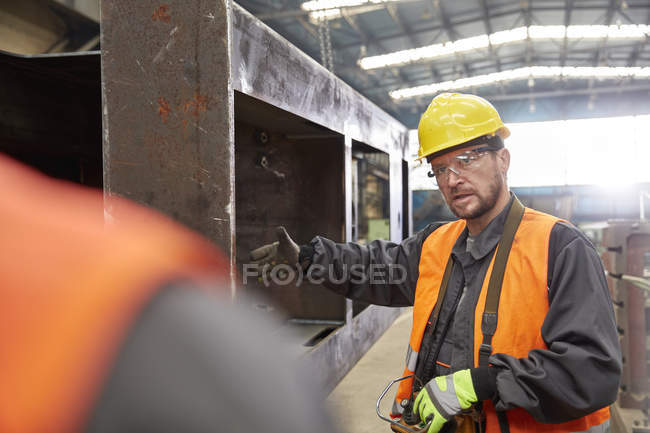 Мужчина жестикулирует, объясняя стальную деталь коллеге на заводе — стоковое фото
