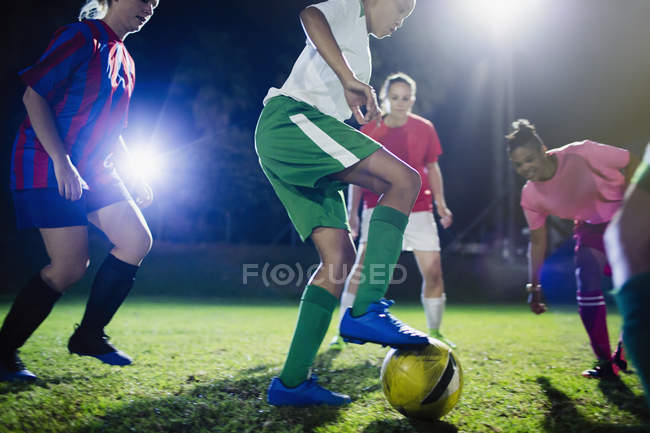 Young female soccer players playing on field at night, kicking the ball — Stock Photo