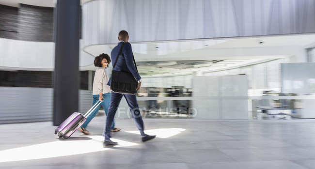 Hombre de negocios y mujer de negocios caminando, tirando de la maleta en el vestíbulo de la oficina moderna - foto de stock
