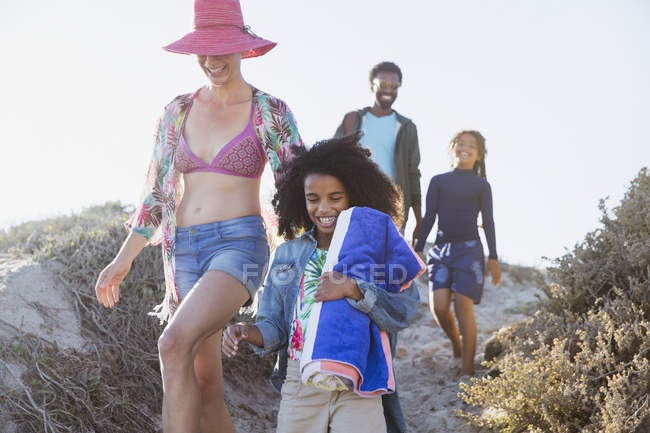 Sonriente familia caminando en la soleada colina de playa de verano - foto de stock