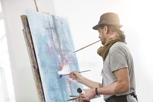 Male artist painting at easel in art studio — Stock Photo