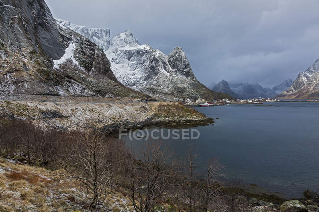 Nevado, montanhas acidentadas ao longo da água, Reine, Lofoten, Noruega — Fotografia de Stock