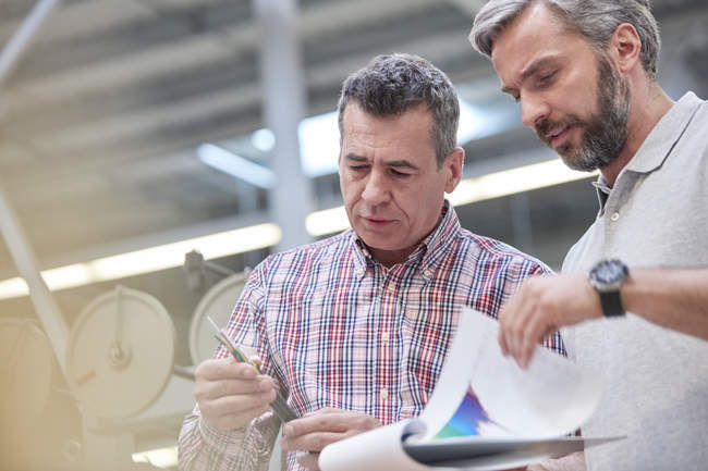 Männliche Vorgesetzte mit Klemmbrett untersuchen Glasfaserkabel in Fabrik — Stockfoto