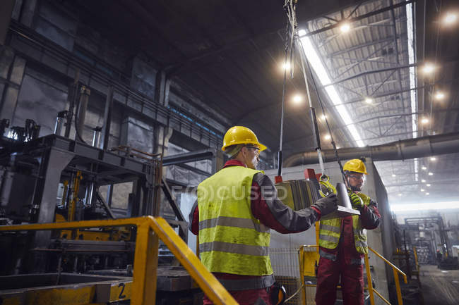 Métallurgistes déplaçant une pièce en acier dans une aciérie — Photo de stock