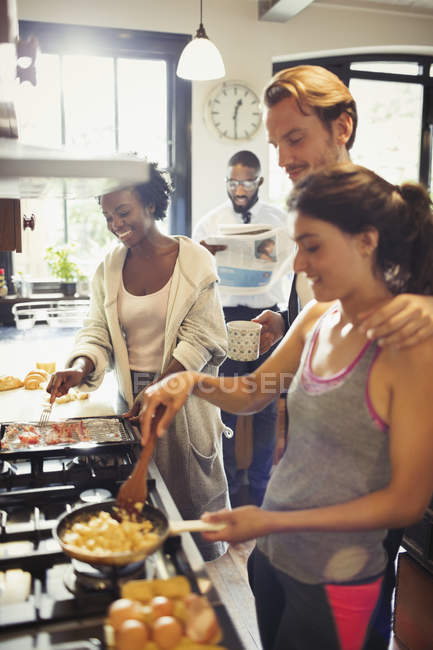 Compañeros de cuarto amigo cocinar huevos revueltos en la estufa en la cocina - foto de stock