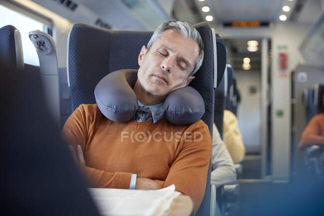 Уставший бизнесмен с подушкой на шее спит в пассажирском поезде — стоковое фото