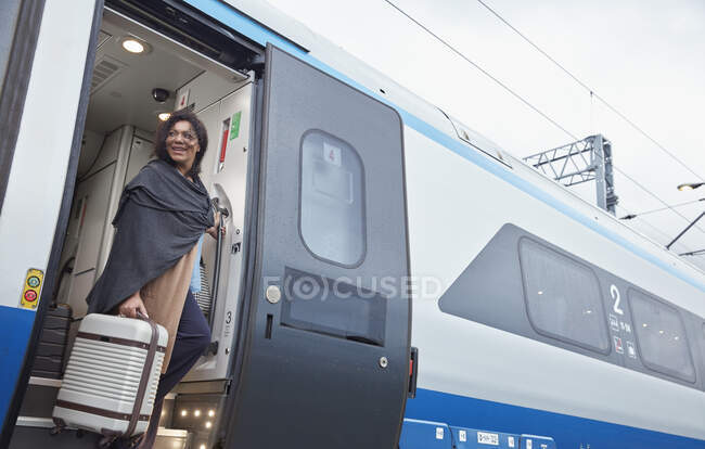 Mujer con maleta bajándose del tren de pasajeros en la estación de tren - foto de stock