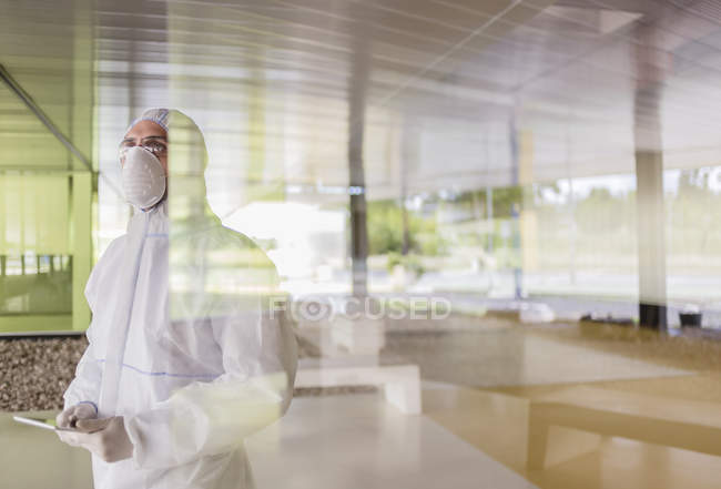 Scientist in clean suit using digital tablet at window — Stock Photo