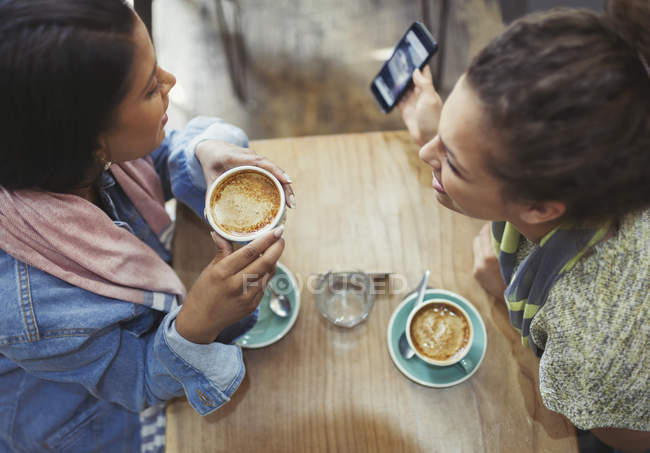 Amigas tomando café y usando el teléfono celular en la cafetería - foto de stock