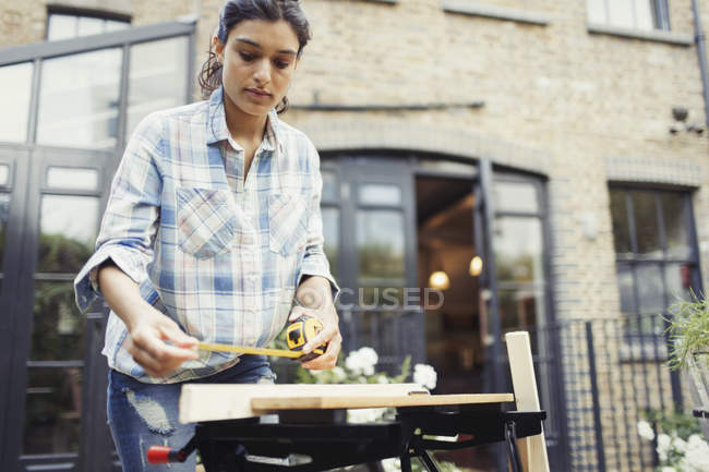 Young woman with tape measure measuring wood on patio — Stock Photo