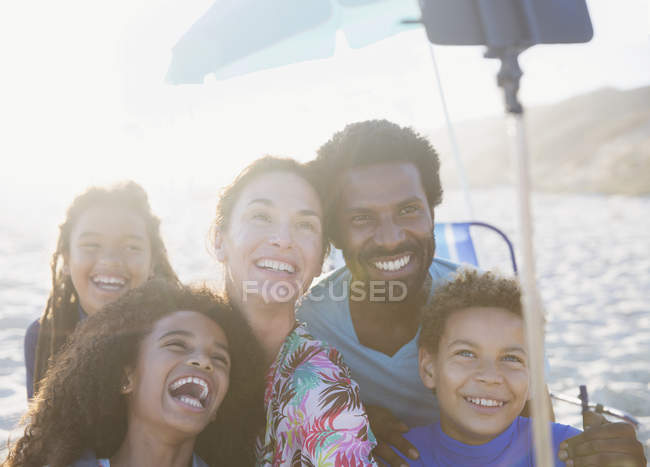 Famiglia multietnica felice e giocosa che si fa selfie con bastone selfie sulla soleggiata spiaggia estiva — Foto stock