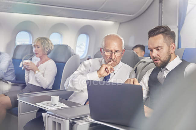 Бізнесмени, що працюють на ноутбуці першого класу на літаку — стокове фото