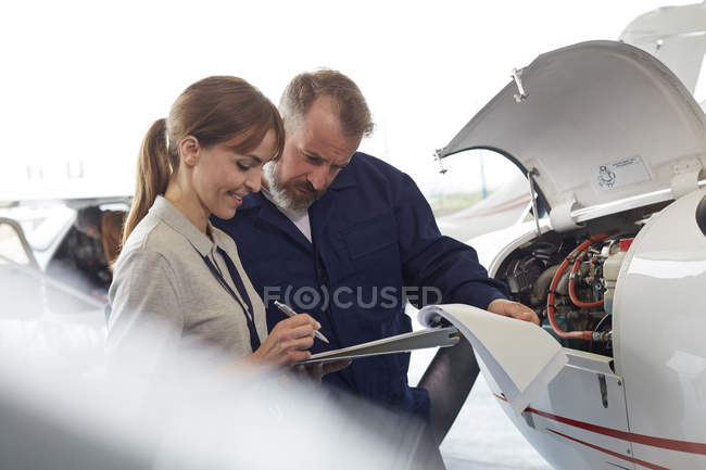 Mechaniker begutachten Papierkram neben Flugzeug im Hangar — Stockfoto
