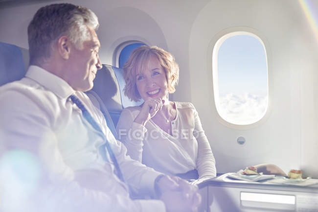 Улыбающаяся взрослая пара ест и разговаривает в первом классе на самолете — стоковое фото