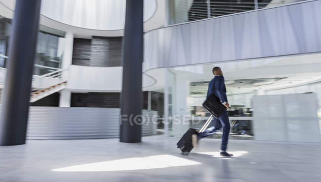 Empresário correndo, puxando mala no lobby de escritório moderno — Fotografia de Stock