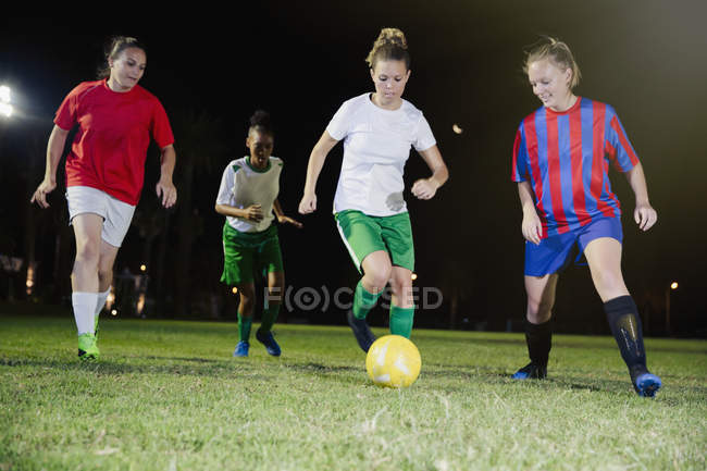 Jeunes joueuses de soccer jouant au soccer sur le terrain la nuit, donnant un coup de pied au ballon — Photo de stock
