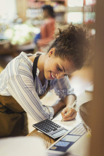 Smiling female cashier using calculator at store counter — Stock Photo