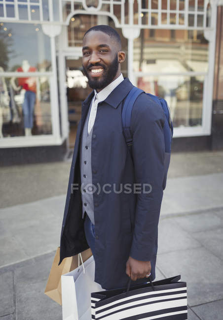 Retrato sonriente, joven seguro de sí mismo con bolsas de compras frente a la tienda - foto de stock