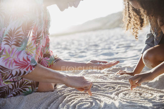 Мать и дочь рисуют спирали на песке на солнечном летнем пляже — стоковое фото