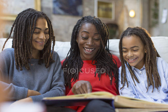 Madre e figlie guardando album fotografico sul divano — Foto stock