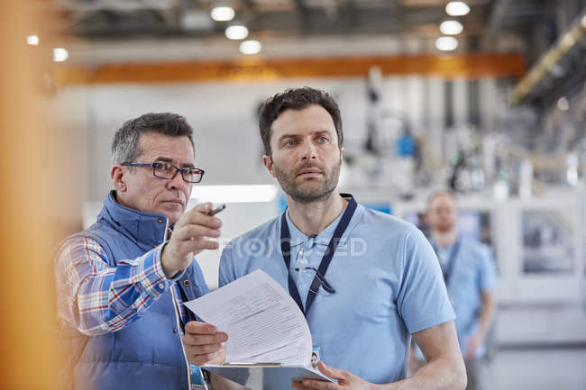 Supervisores masculinos serios con portapapeles hablando en fábrica - foto de stock