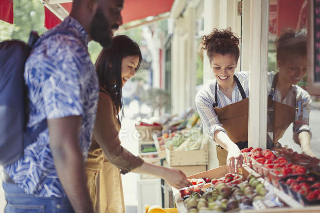 Рабочий помогает паре покупать фрукты на тротуаре магазина — стоковое фото