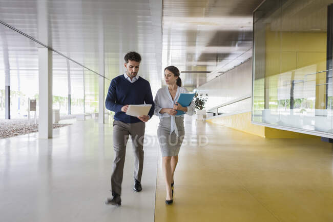 Businessman and businesswoman walking and discussing paperwork in modern office corridor — Stock Photo