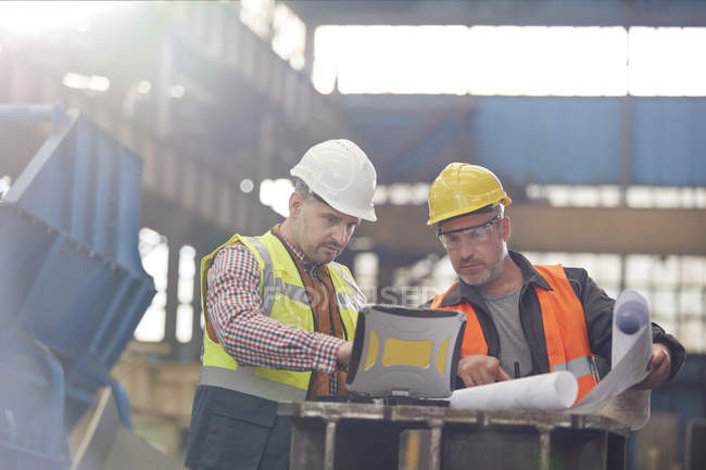 Male foreman and engineer working at laptop with blueprints in factory — Stock Photo