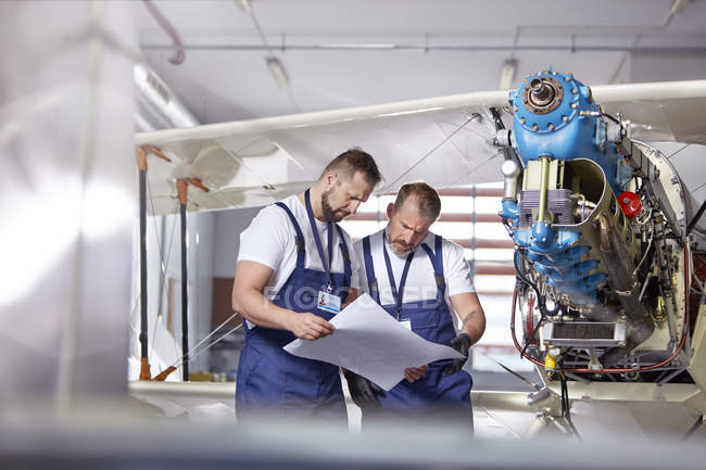 Male engineer mechanics examining plans, fixing airplane in hangar — Stock Photo