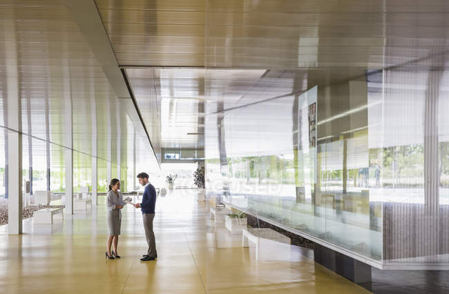 Businessman and businesswoman talking in modern office lobby corridor — Stock Photo