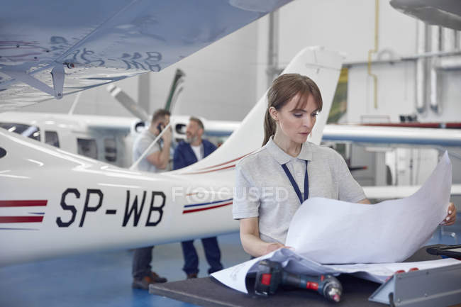 Ingegnere meccanico donna che esamina i piani in hangar aereo — Foto stock