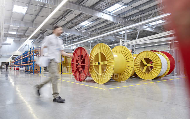 Male worker walking by large spools in fiber optics factory — Stock Photo